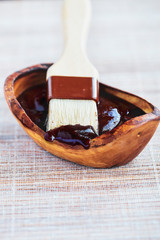 BBQ sauce on the tip of a basting brush with a wooden bowl filled with the condiment. Selective...