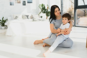 Obraz premium Young mother with her 4 years old little son dressed in pajamas are relaxing and playing in the bed at the weekend together, lazy morning, warm and cozy scene.