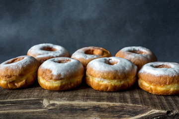 Lush sweet homemade donuts sprinkled with powdered sugar on a wooden background