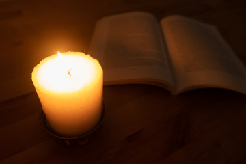 Candle burning brightly with book in background. Close up, shallow depth of field.