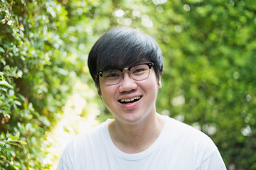 An Asian man aged about 30 years old, looking good, wearing glasses, wearing a white T-shirt Sitting in a small garden at home