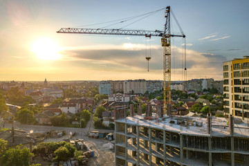 Apartment or office tall building under construction. Brick walls, glass windows, scaffolding and concrete support pillars. Tower crane on bright blue sky copy space background.
