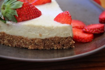 A slice of cheesecake with strawberries on dark triangle plate and wooden table. Extreme closeup, macro, horizontal.
