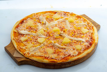 Hawaiian pizza on a wooden board with pineapple and chicken filet