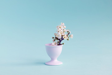 Still life of bouquet of blooming cherry plum in a makeshift vase and an egg stand. White-gray neutral background. Copy space.