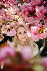 Portrait of young woman in park with blooming sakura trees.