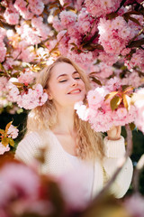 Fototapeta premium Portrait of young woman in park with blooming sakura trees.