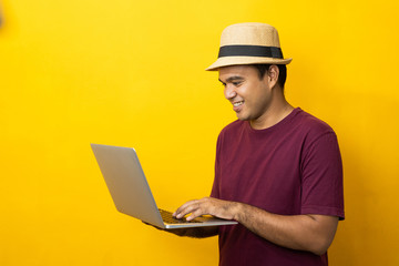 Asian man red shirt with hat using laptop on isolated yellow background.