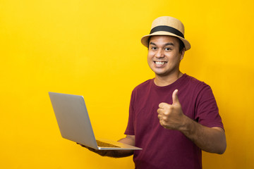 Asian man red shirt with hat using laptop on isolated yellow background.