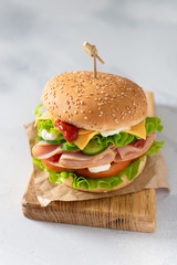 Delicious sandwich with fresh vegetables, cheese and ham on wooden board on gray background. Side view, close up. Menu, recipe