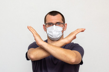 A man with glasses in a protective medical mask standing with crossed hands indoor on white...
