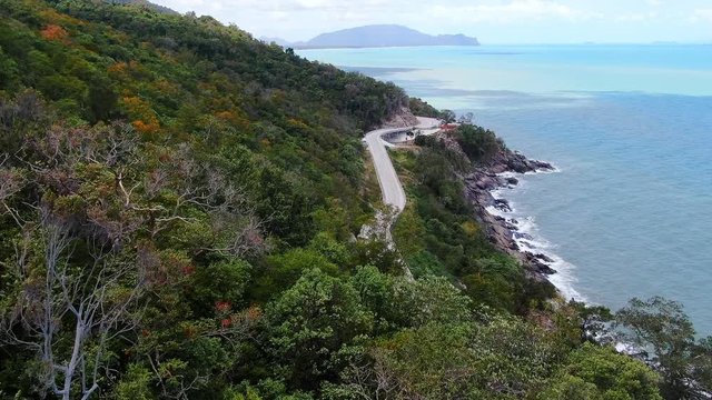 Aerial view of Slow motion and following video of car running on the road beside the sea at southern of thailand. with autumn mountain in summer season. smooth drone shot.