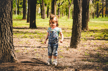May 2020. Kiev Ukraine. A little girl plays outside in a park, collects plants on a sunny day in denim overalls and a T-shirt with a print  LOL