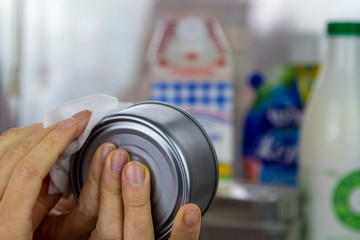 A woman washes a tin of canned food using an antiseptic napkin. Disinfection of products bought in the supermarket during the coronavirus epidemic.