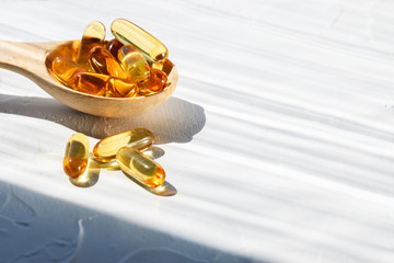 Omega 3 capsules in the wooden spoon on white concrete background, hard shadows, copy space for...