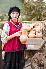 Beautiful girl in national dress. Holding an ancient pot in his hands. Antique clothing of the late 19th century. Beautiful dress and skirt on a woman. The concept of rural life, national traditions