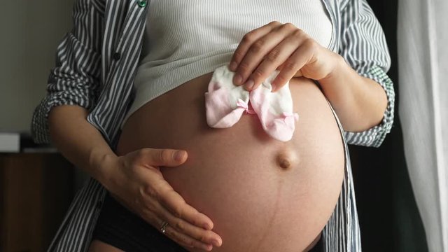 Pregnant woman feeling happy expecting mother holding pink litle socks