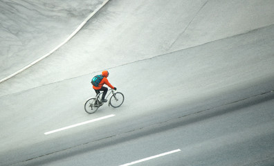 A cyclist in a red jacket with a backpack rides on an asphalt road