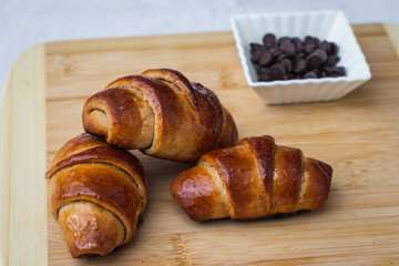homemade whole spelled flour croissants, on a wooden surface, next to chocolate chips in a small ceramic square bowl, selective focus.