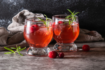 Refreshing non alcoholic cranberry tea with ice and rosemary on dark marble table. Summer cold drink. Healthy vitamin drink on the table.