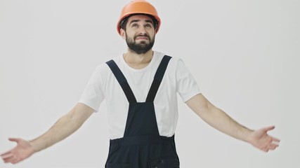 Confused young bearded man builder isolated over white wall background in helmet
