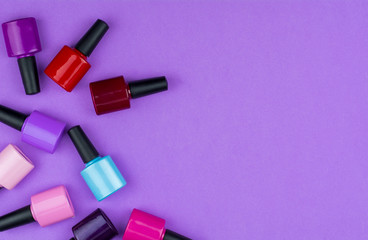 Color nail polish bottles on violet background composition.