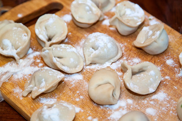 Fototapeta na wymiar Raw homemade dumplings with minced meat on wooden board on table, sprinkled with flour. Close up view of traditional Russian pelmeni. Selective focus