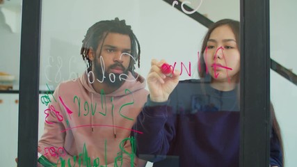 Positive diverse multiracial business team drawing financial trends and stock market data on transparent glass board with markers, brainstorming business strategy and sharing visions at home office. - Powered by Adobe