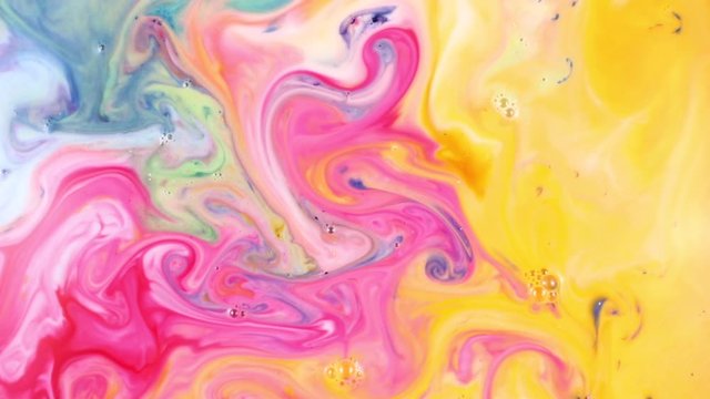 Close-up view of mixture of bright multi-colored paint in milk. Abstract beautiful pink yellow and blue colors of the liquid are mixed together, spilled and dissolved in white paint for the designer.