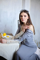 The girl at the table touches her bare shoulder with her fingers and waits for her lover. Romantic date. Bride with a crown on her head. A gorgeous brunette in an evening dress.