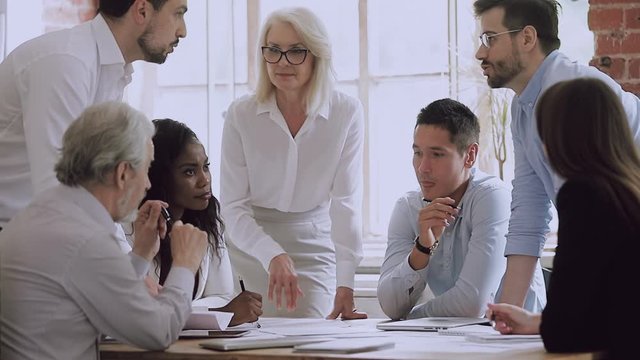 Confident mature business team leader discussing project ideas together with diverse colleagues, does not agree with points of view, upholding personal opinion at brainstorming meeting in office.