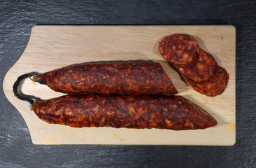 Photography of a cut chorizo and slices on a wooden board on slate background for food illustration