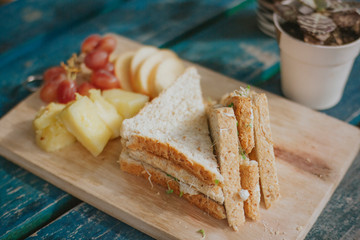A sandwich cut in half with fruits on a wood panel. Rustic.