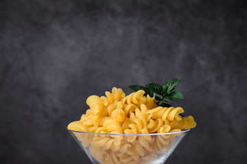 Raw uncooked italian pasta on cocktail glass over white marble. Fusilli. Diet and food concept. Copy space.