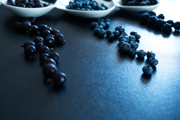 Set of different types of black berries in a white plate on a black table. Stylish seasonal vitamins