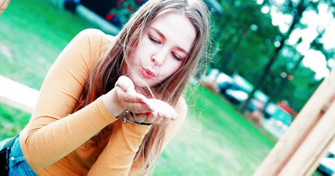 Young caucasian hipster girl blowing glimmer at festival site in slow motion