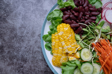 bowl of salad with vegetables ,fresh green oak salad, tomatoes, corn, Red beans, Carrot , red radish, olive oil and cucumber on white marble table. Top view. Food Concept for healthy diet
