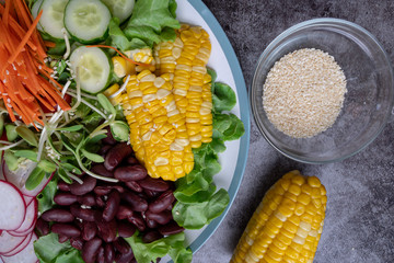 bowl of salad with vegetables ,fresh green oak salad, tomatoes, corn, Red beans, Carrot , red radish, olive oil and cucumber on white marble table. Top view. Food Concept for healthy diet