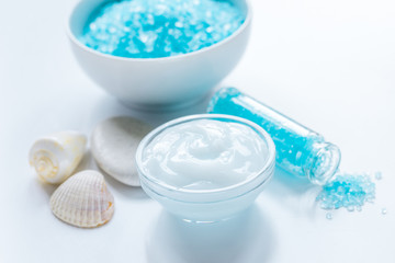 blue bath salt, body cream and shells for spa on white table background