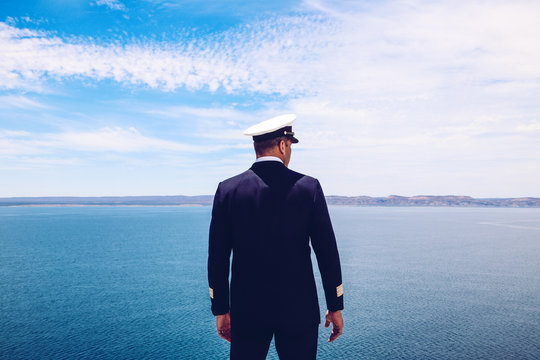 Strong posture of a captain looking at the sea and faraway land on the horizon. Navy/Cruise ship concept. Outdoor shot.