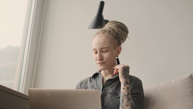Young serious amazing girl with dreadlocks indoors using laptop computer