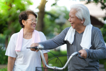 
A senior couple is happily riding their bicycles in the park in the morning.