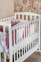 Fototapeta na wymiar Baby bed crib with white and burgundy color pillows with laces