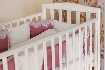 Fototapeta na wymiar Baby bed crib with white and Burgundy color pillows with laces
