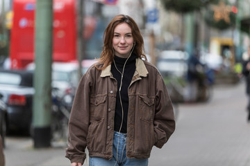 Happy Young Woman Listening to Earphones on Sidewalk