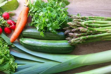 Various vegetables and herbs on a table: leek, lettuce, asparagus, parsley, carrot and radish. Top view.