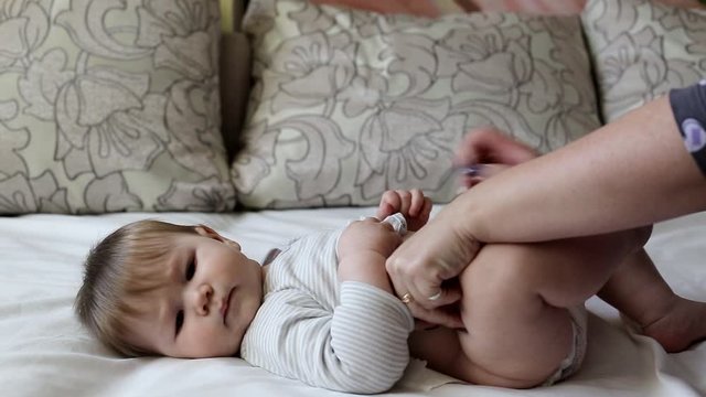 mother dresses diaper to little caucasian baby boy, Little boy aged 8 months, brown-eyed