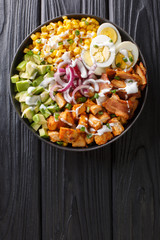balanced salad of chicken, avocado, corn, onions, eggs and bacon with yogurt dressing closeup in a plate. vertical top view
