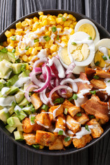 Fresh salad of chicken, avocado, corn, onions, eggs and bacon closeup in a plate. vertical top view