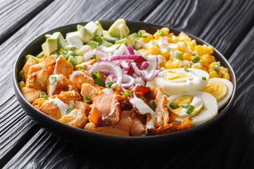 Hearty salad with avocado, chicken, corn, onion, eggs seasoned with yogurt closeup in a plate on the table. horizontal